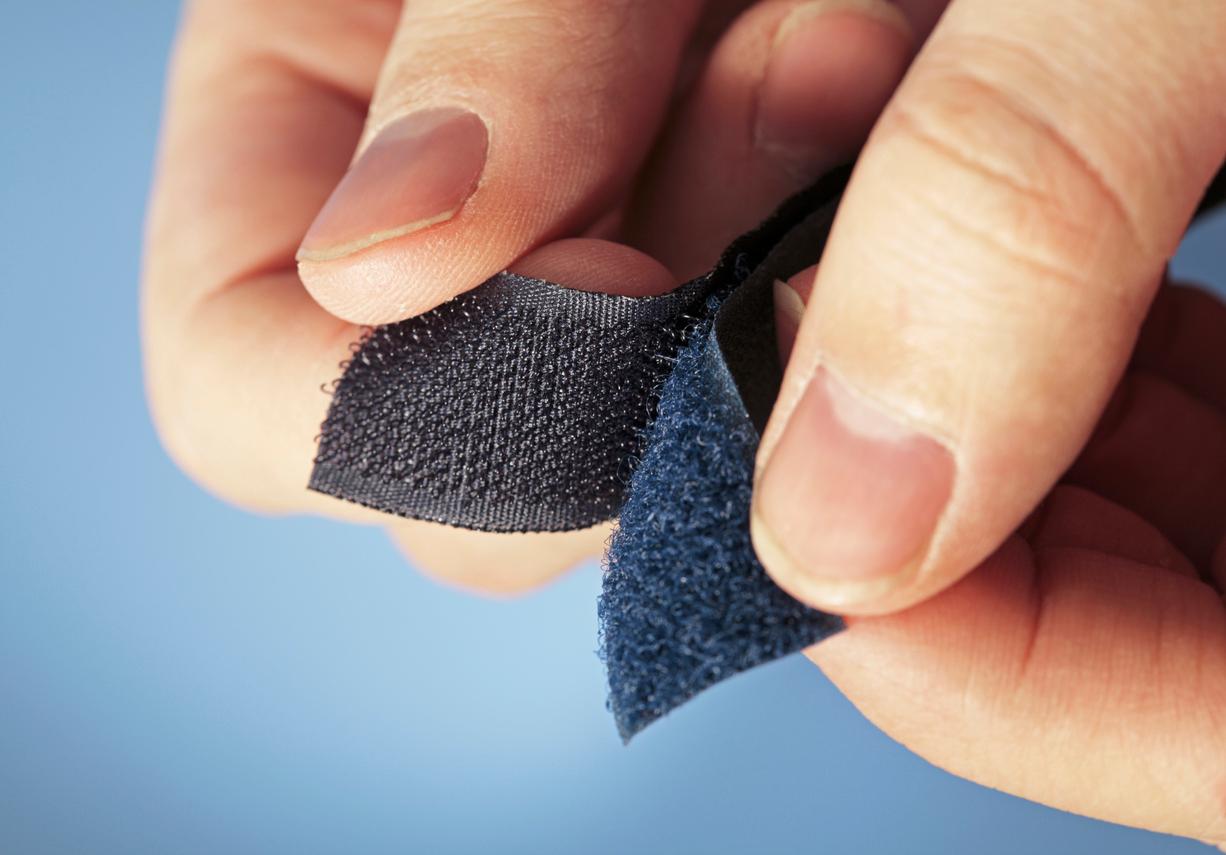 A close up of two sides of Velcro being pulled apart against a light blue background. 