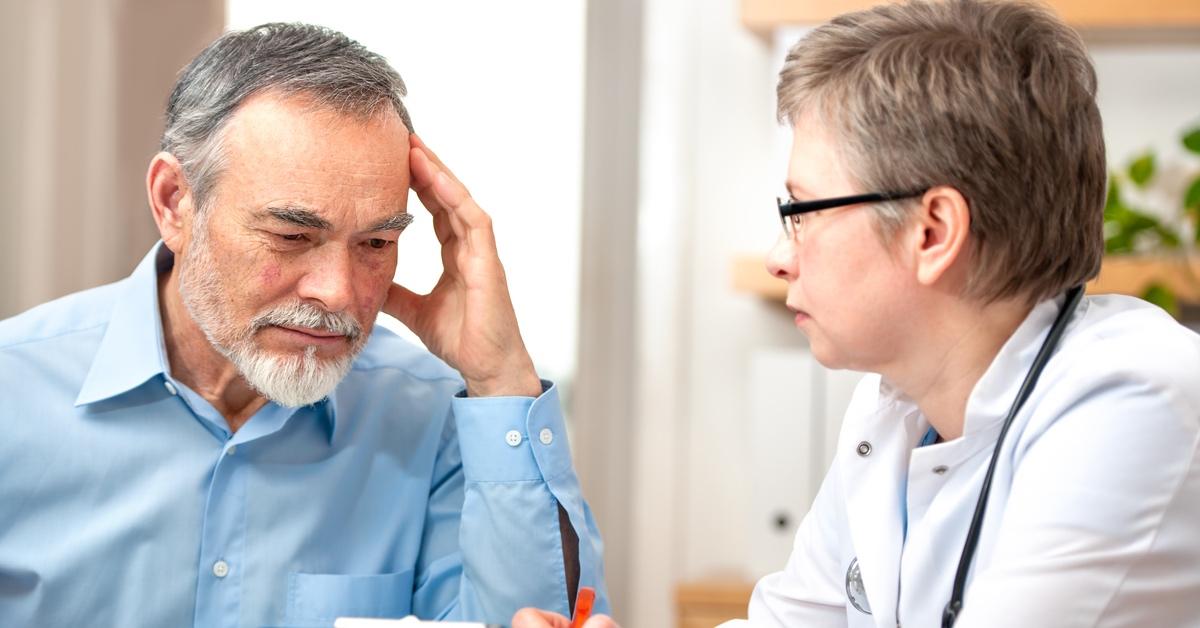 Elderly man holding his head speaking with a doctor.