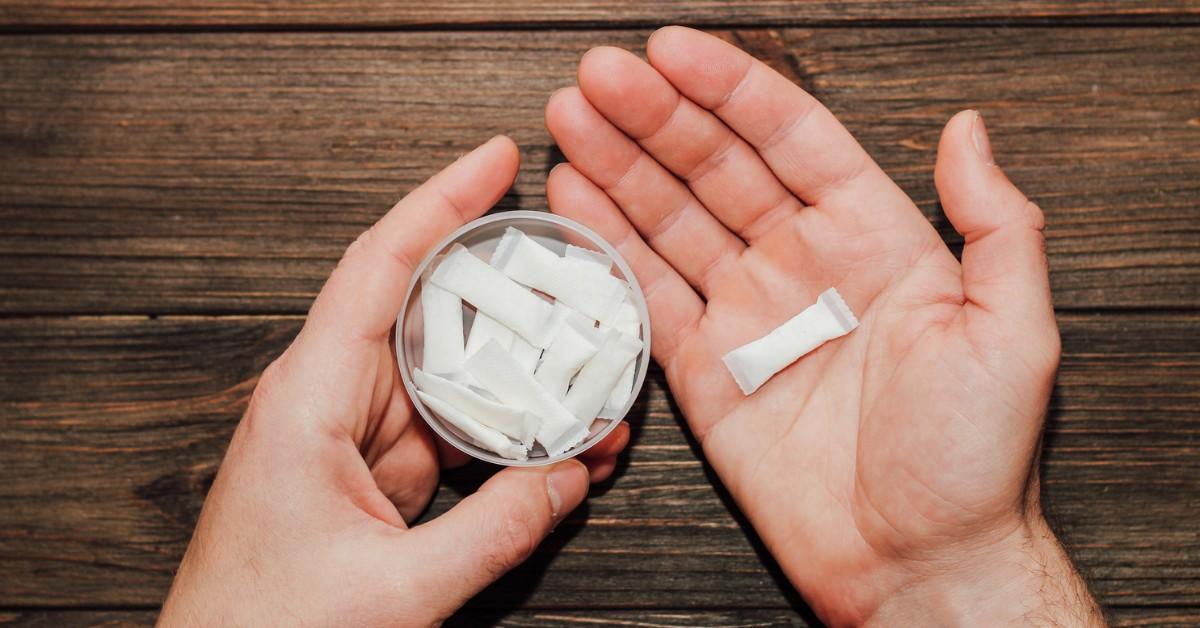 A man holds a nicotine patch in the palm of one hand and a container of pouches in the other