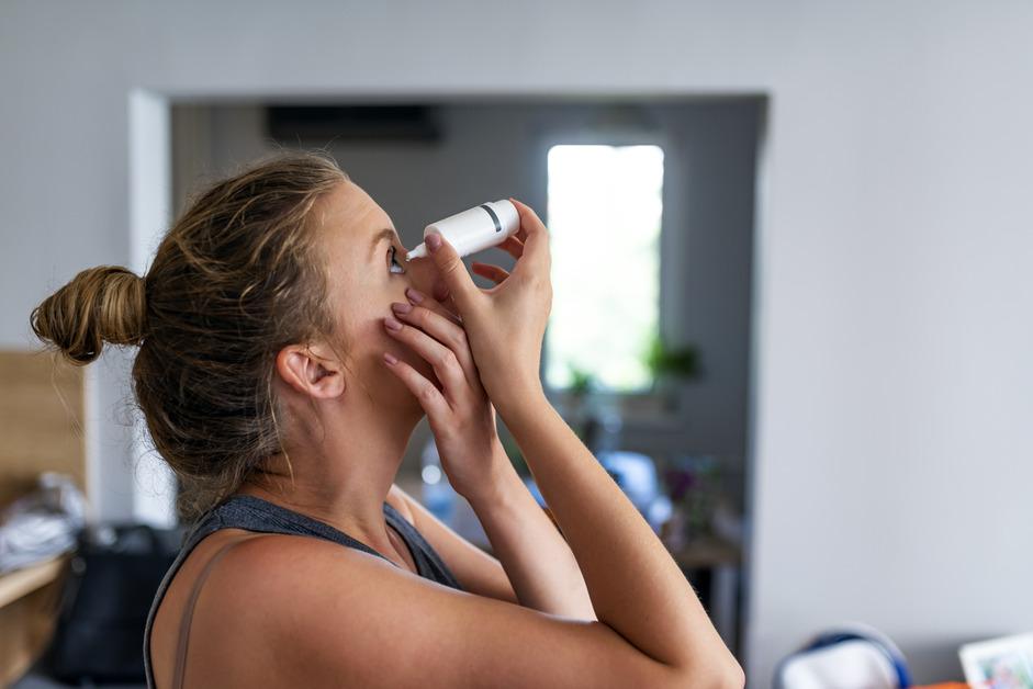 A woman with a bun in her hair holds her eye open while using eye drops. 