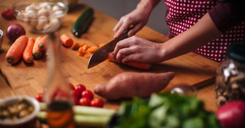 A person chops a carrot on a butcher block, alongside various other raw vegetables.