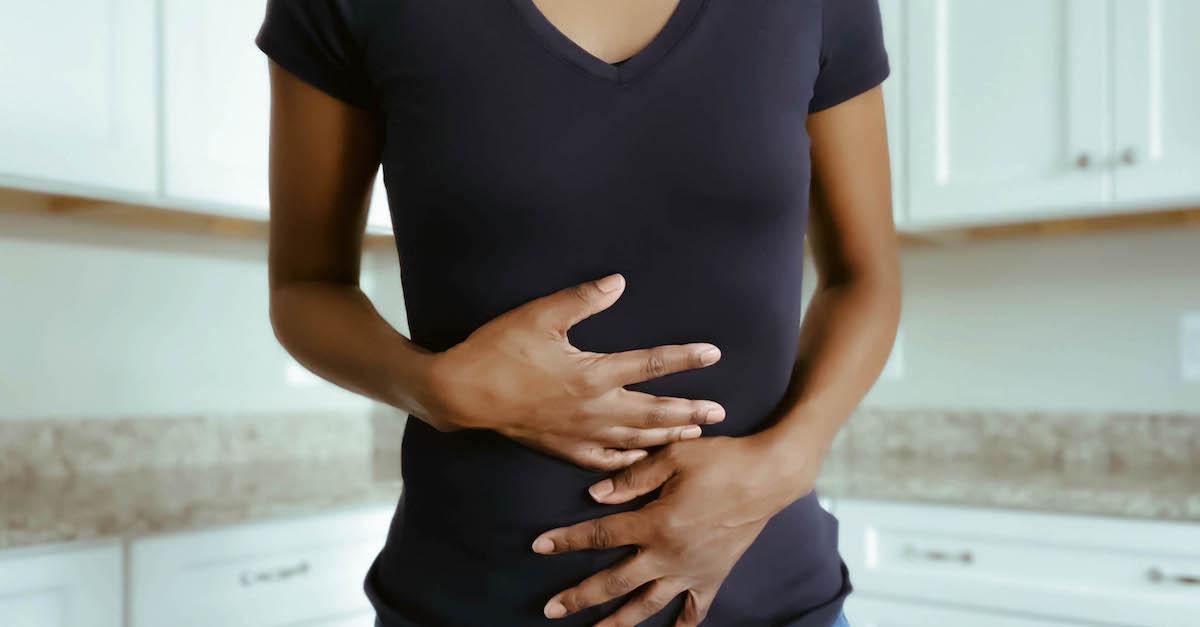 Woman stands in a kitchen and holds her stomach