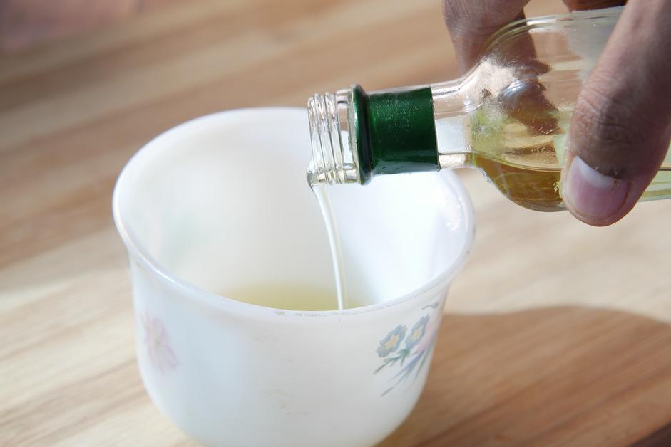 A person pours white vinegar into a small bowl.