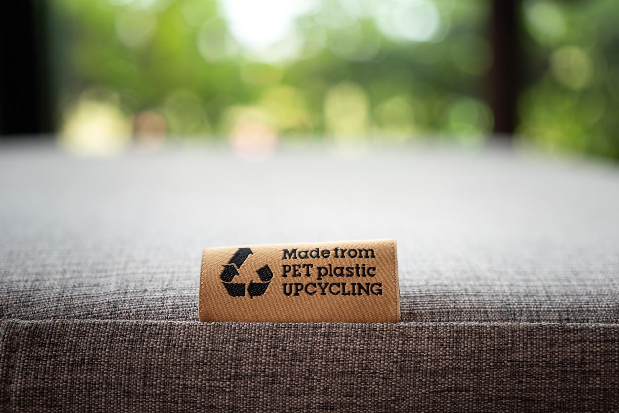 A "Made From PET Plastic Upcycling" product label tag is pictured on a sofa seat.