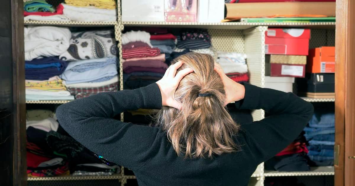 Woman looking into a cluttered closet holding her head in a state of overwhelm 