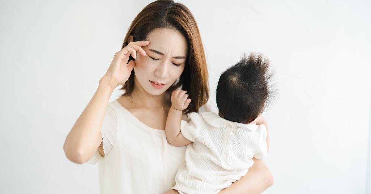 A new mother grabs her head while holding her baby.