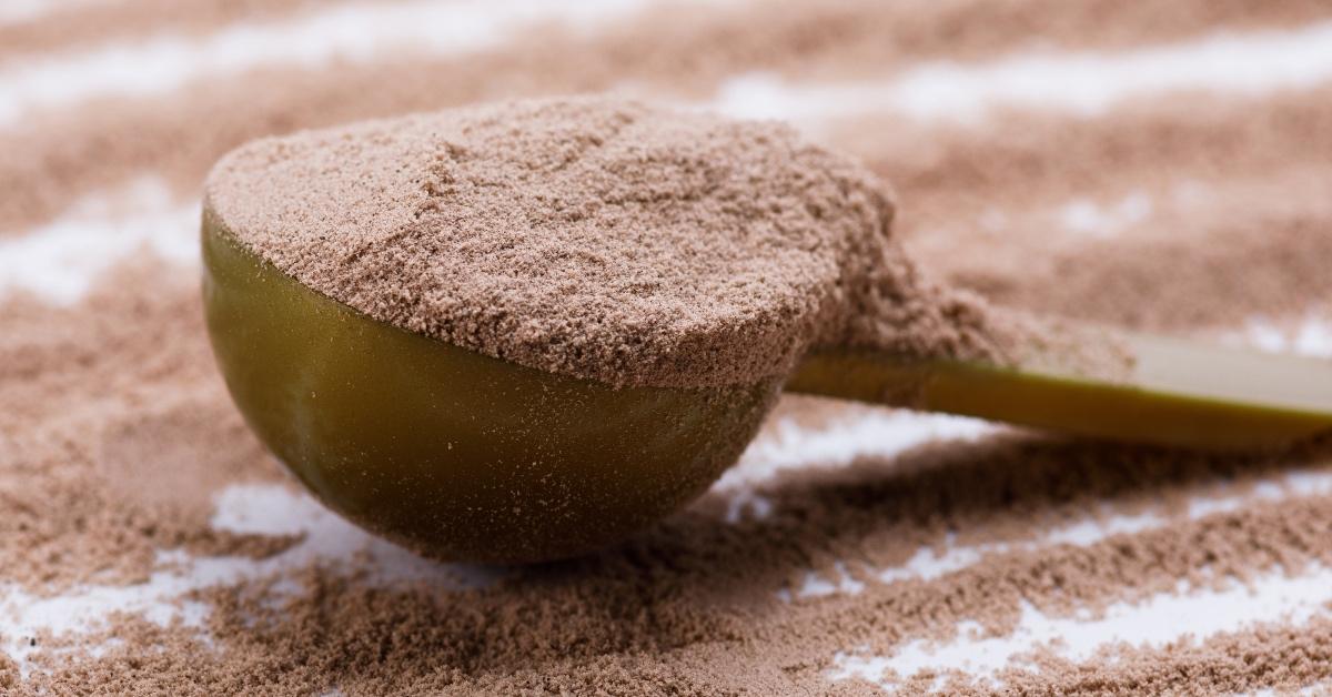 A cup of brown protein powder in a metal measuring cup. 