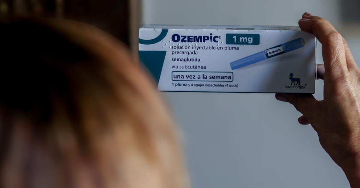 A woman holds up a box of Ozempic medication. 