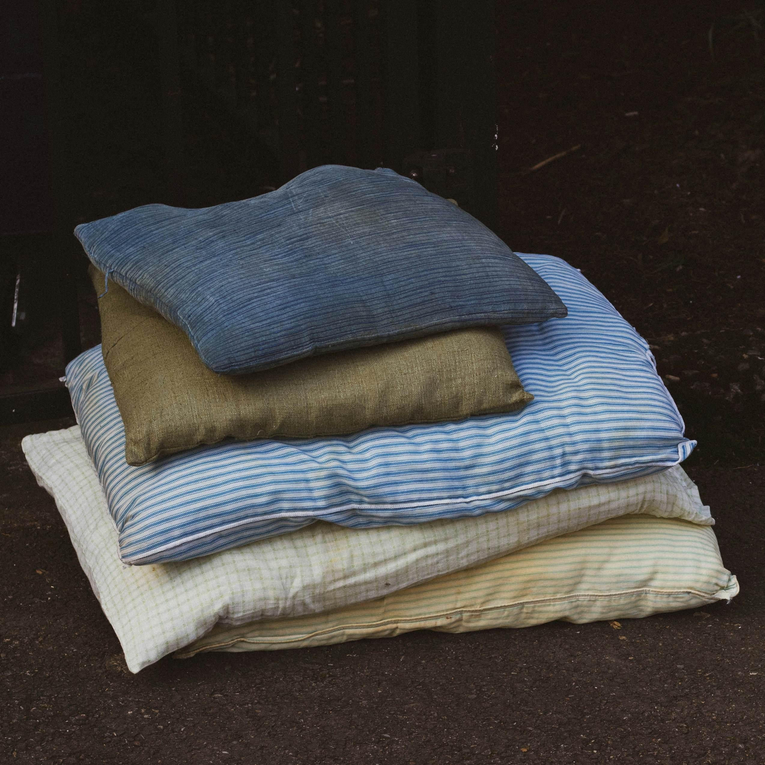 Dirty, yellowed pillows of varying sizes are stacked atop one another against a black background.