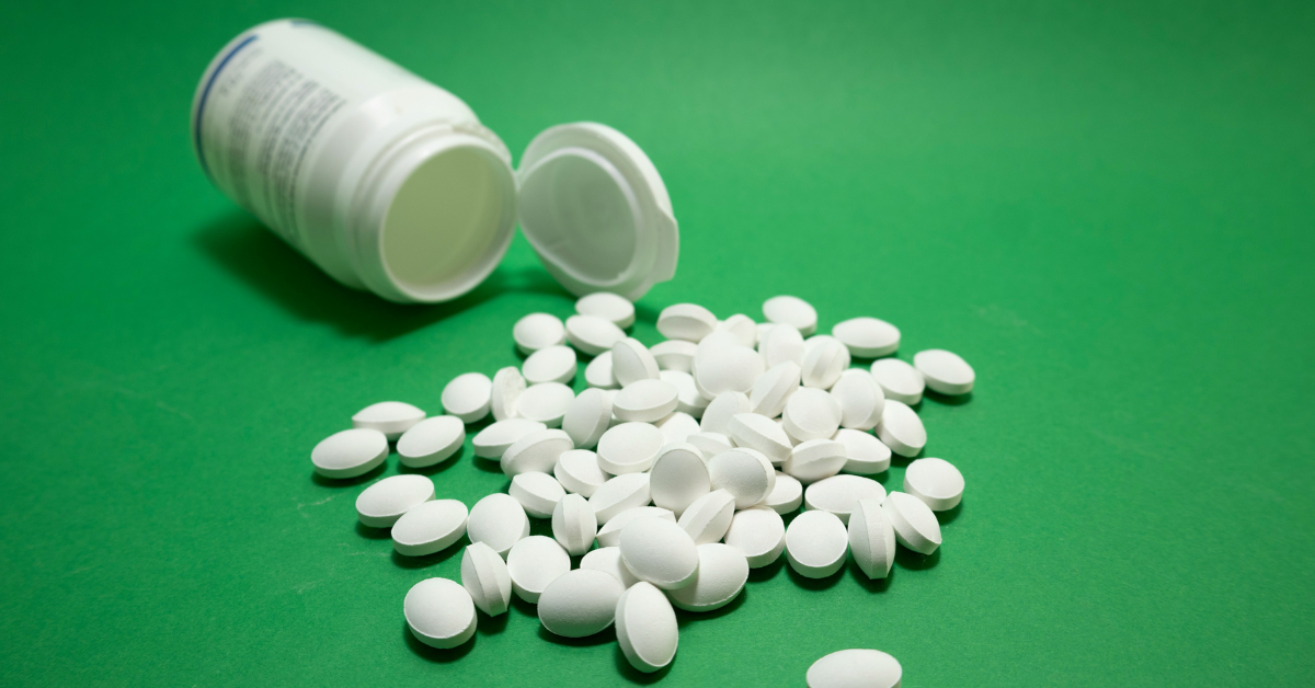 A bunch of white pills spills out onto a green background