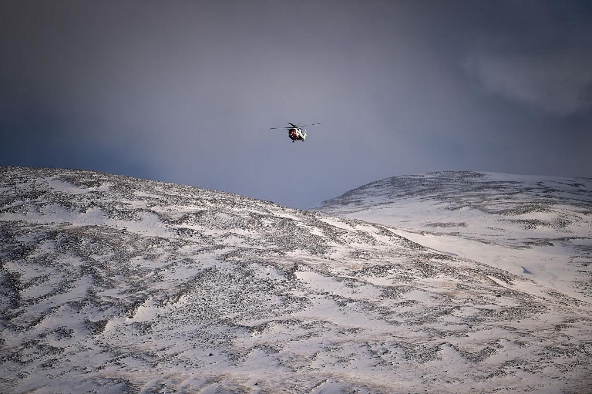 A helicopter flies over a snowy mountain. 