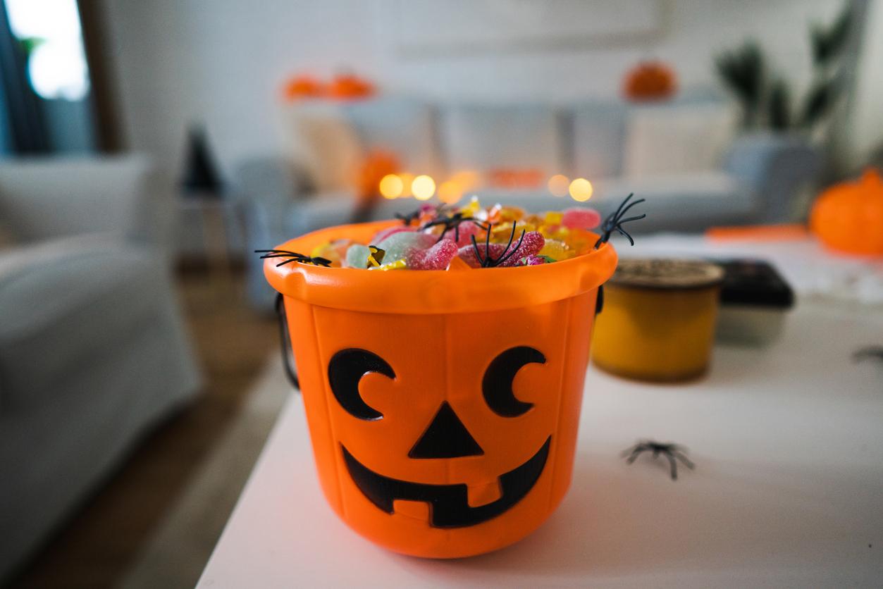 Traditional plastic, pumpkin trick-or-treating bucket filled with various gummy candy.