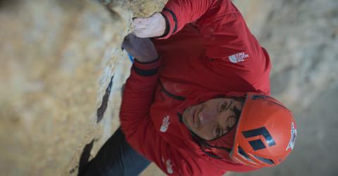 Closeup of Alex Honnold leading the pool wall ascent, wearing red jacket and helmet.