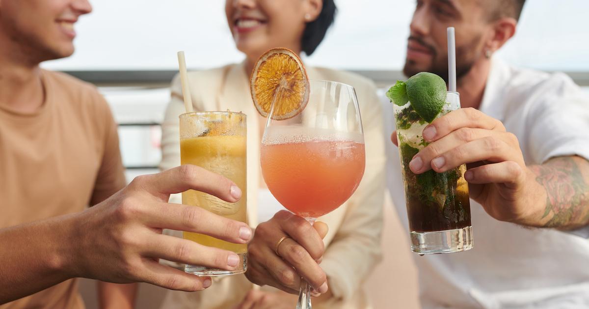 Three people toasting colorful cocktails.