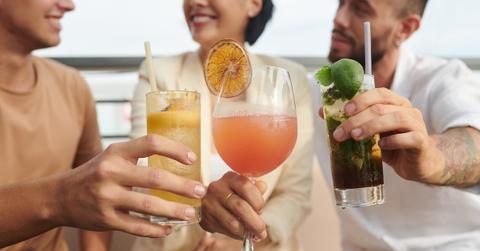 Three people toasting colorful cocktails.