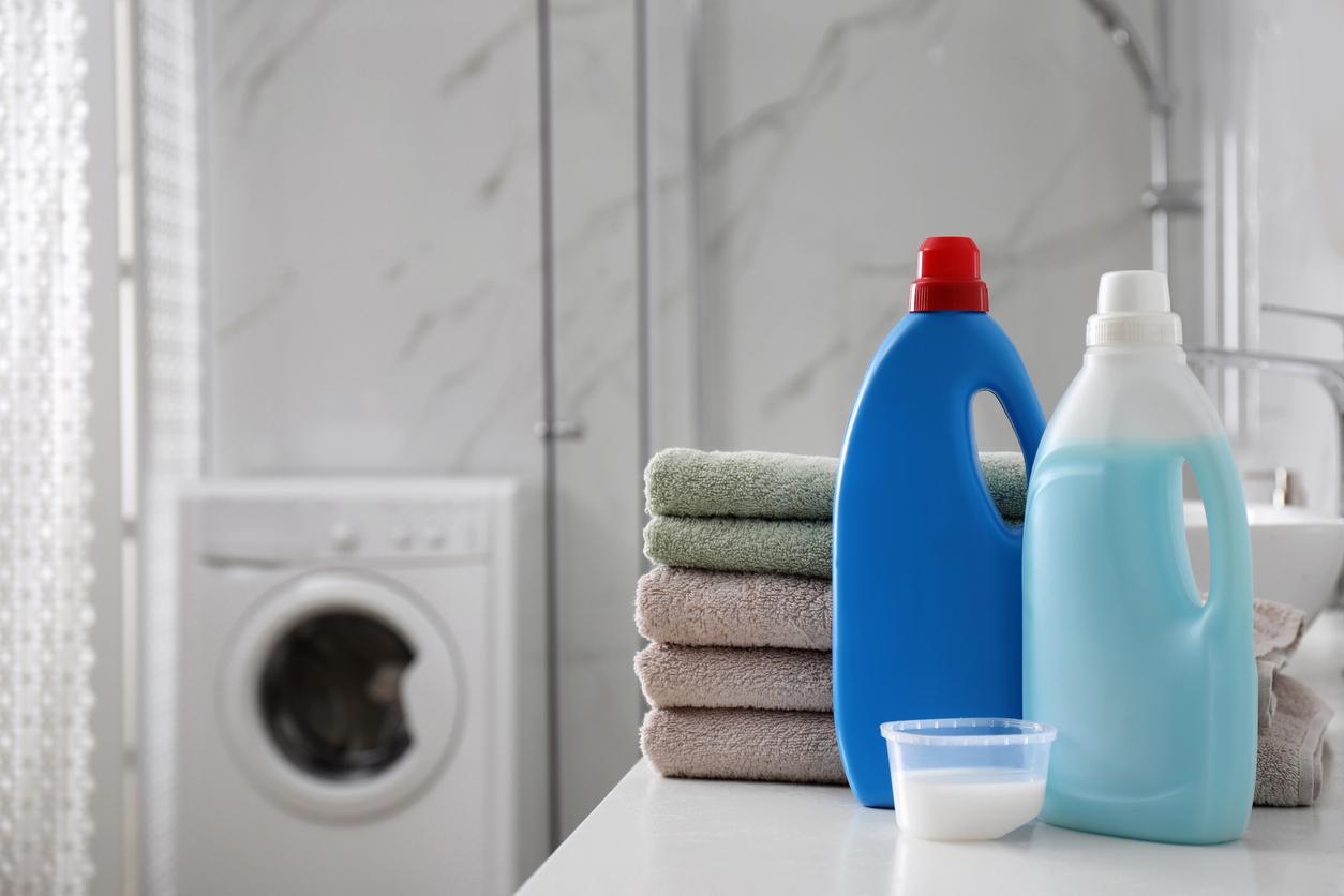 Generic detergents sitting atop a counter next to some towels in a laundry room.