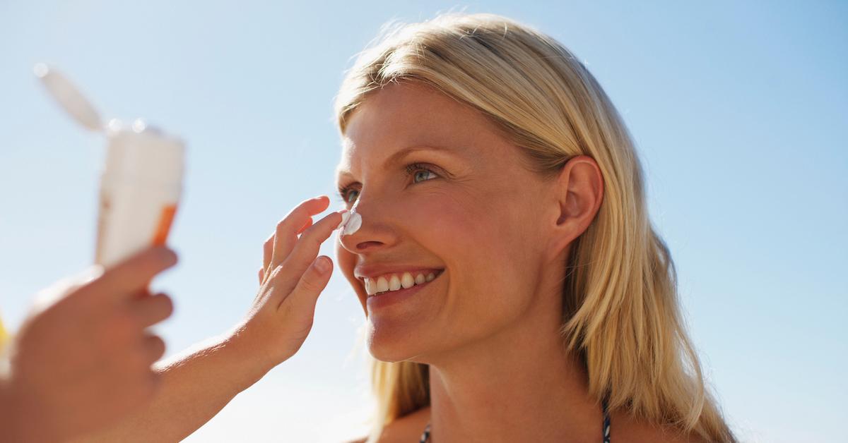 A child applies sunscreen to the face of a blonde woman