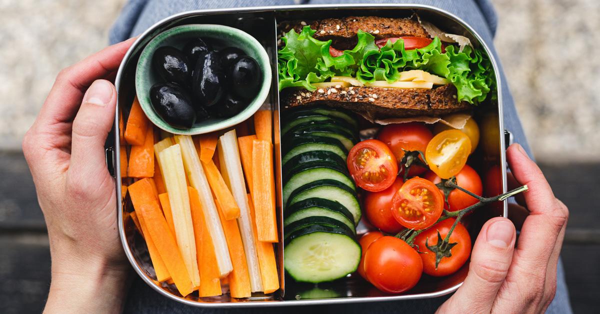 hands holding a stainless steel eco friendly lunch box filled with food.