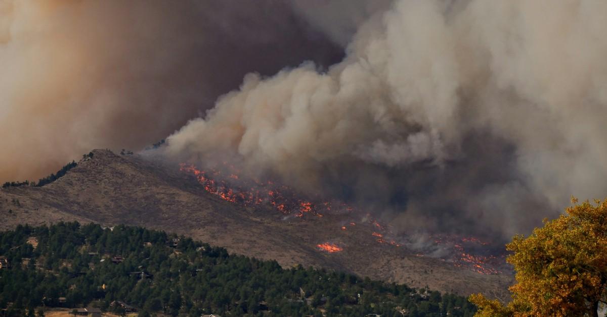 A mountain side burns out of control in the distance as smoke pours into the air