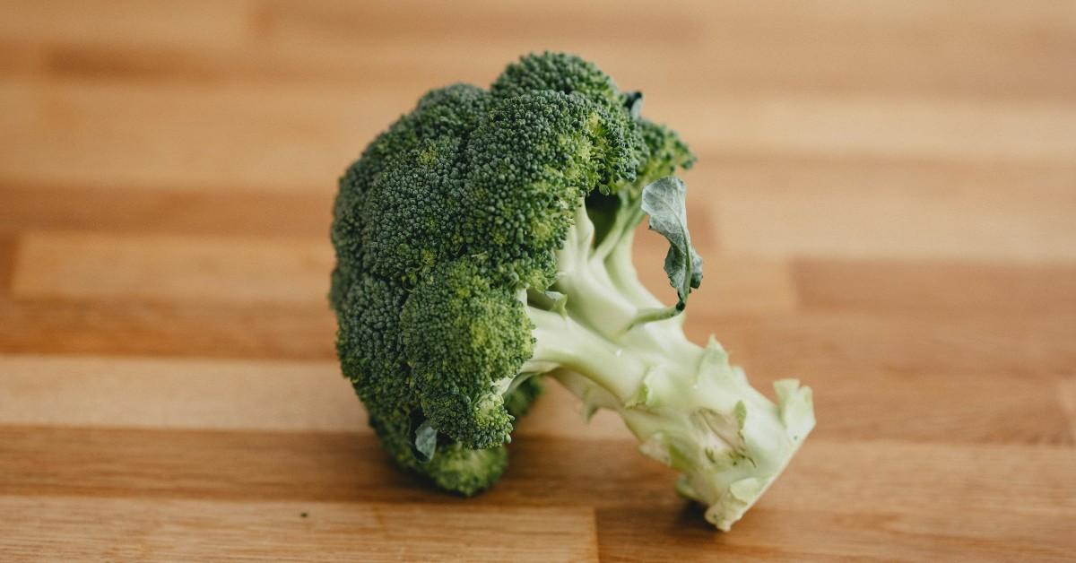 A lone broccoli floret sits on a wood cutting board