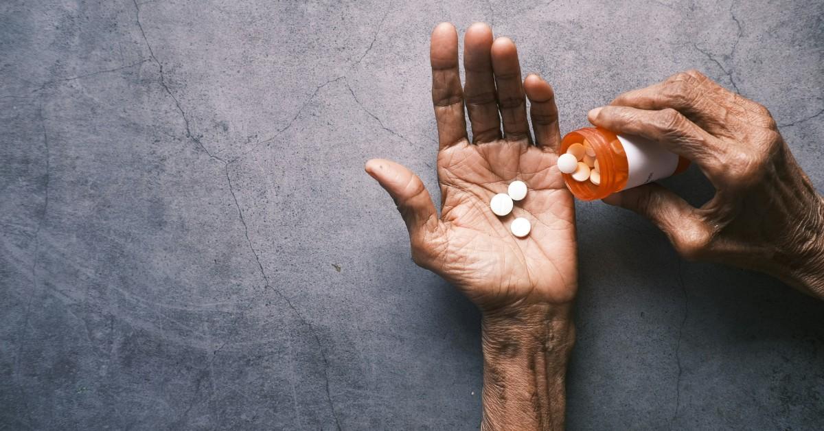 A person holds out their hand while shaking pills out of a prescription bottle