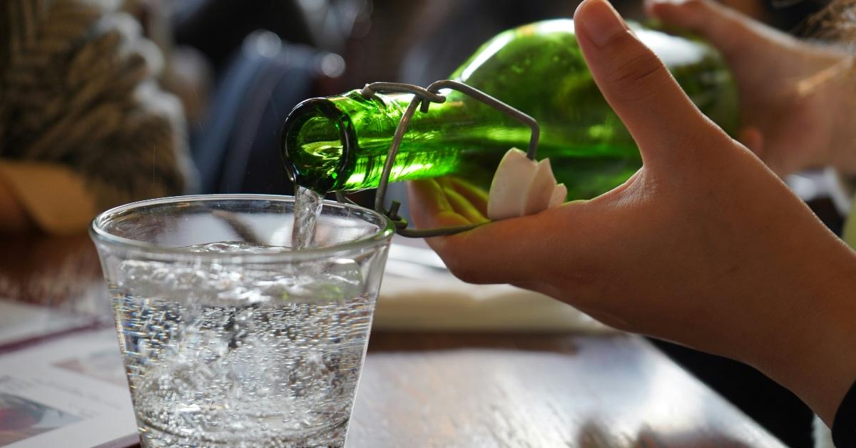 Person pouring a glass bottle of water into a clear cup at a restaurant. 