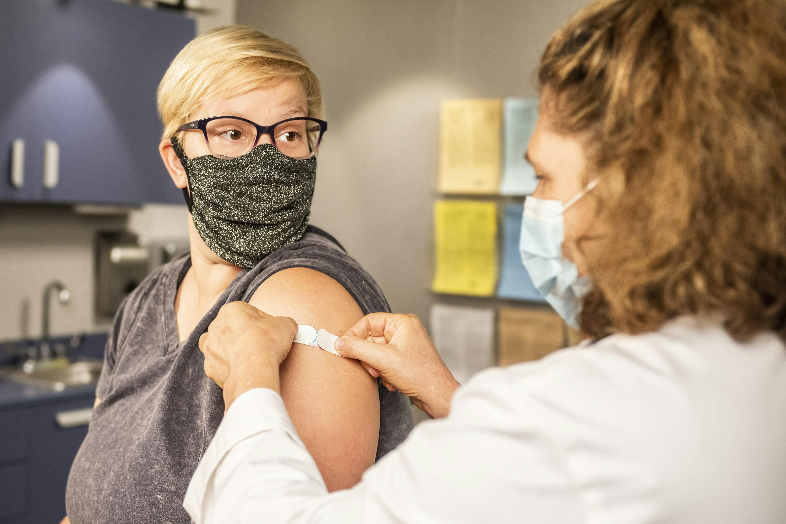 A woman with a glittery face mask receives a bandage after getting the COVID-19 vaccine.