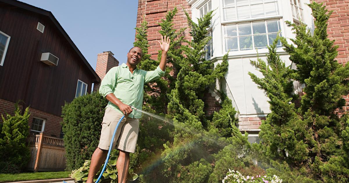 A man waves while watering bushes with a hose 