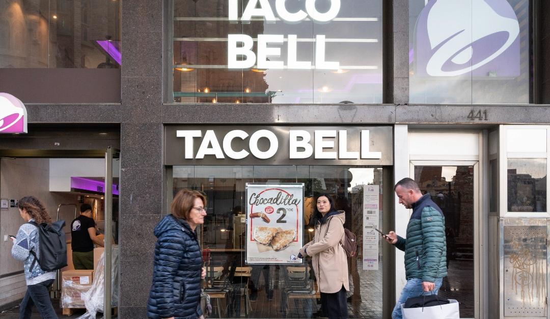 Four pedestrians walk past a Taco Bell in winter coats 