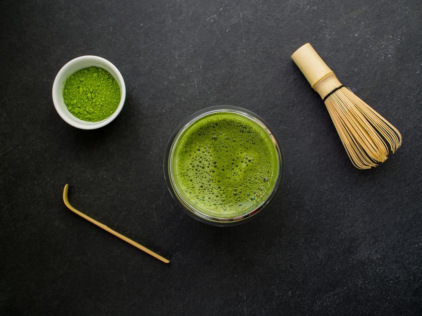 An overhead photo of matcha powder, a matcha drink, a wooden mixer and a wooden whisk.