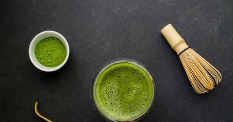 An overhead photo of matcha powder, a matcha drink, a wooden mixer and a wooden whisk.