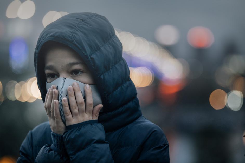 A child holding their face mask in a city with poor air quality. 