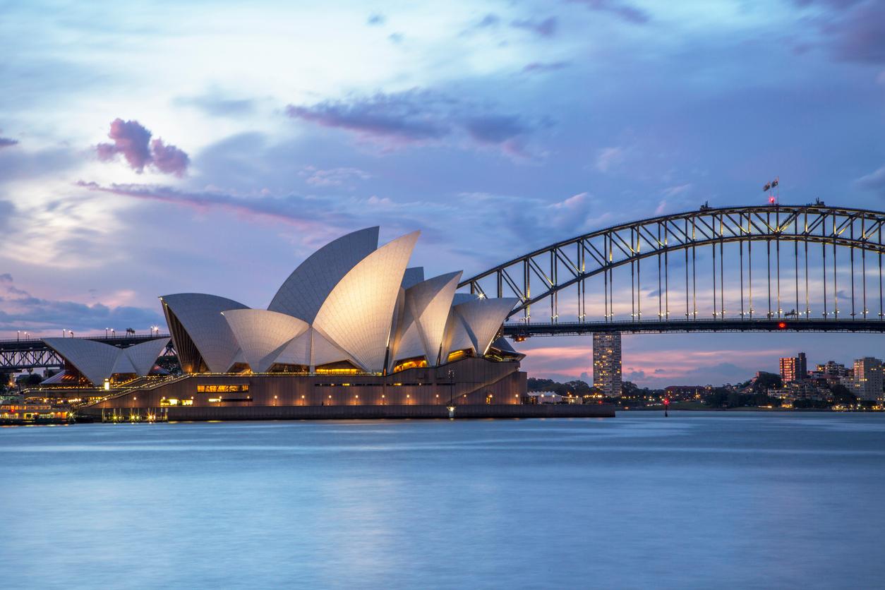 The Sydney Opera House and the Sydney Harbour Bridge in Australia are surrounded by water at dusk.