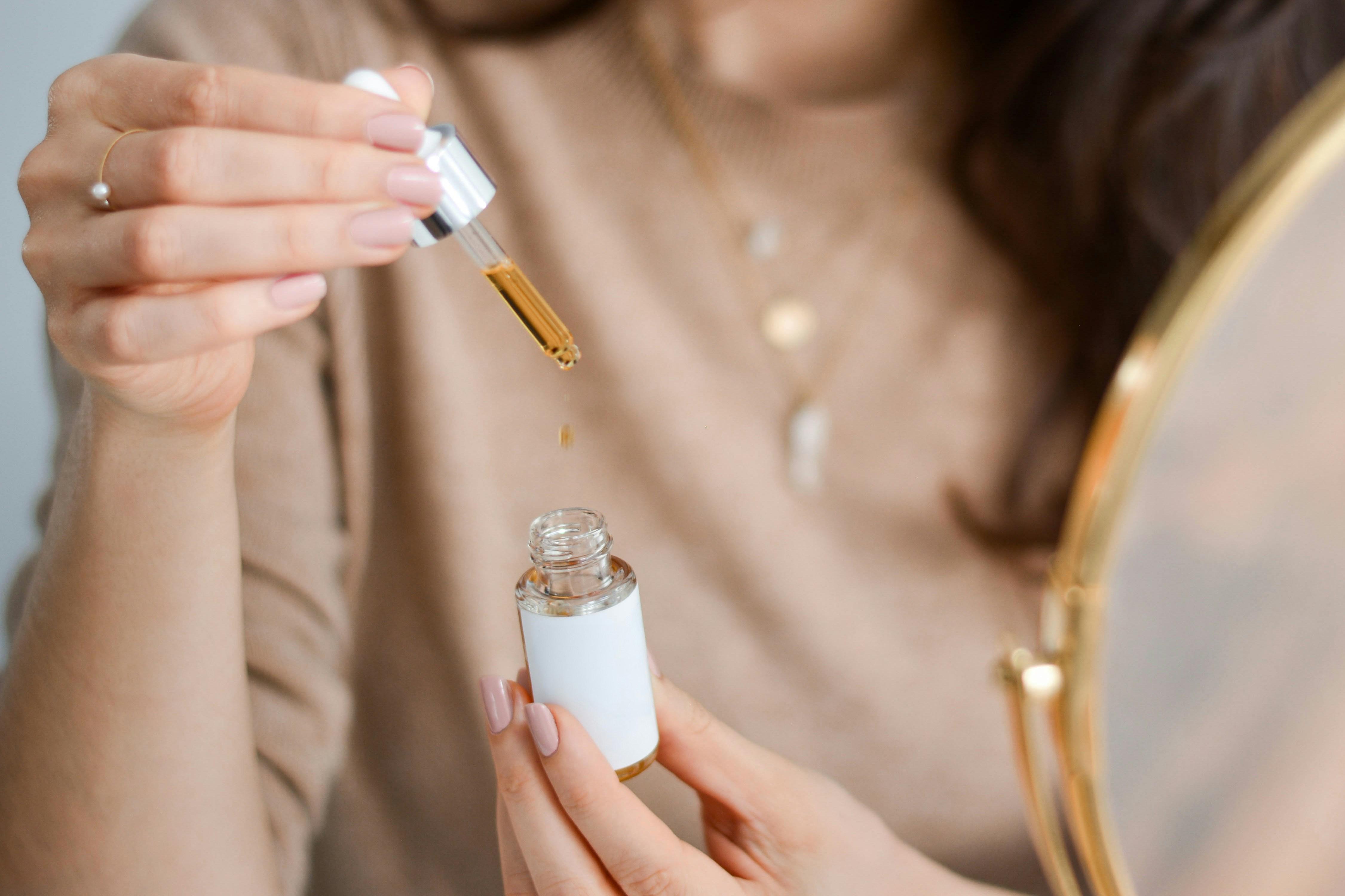A teen girl is pictured from the neck down while holding a bottle of serum and a dropper.
