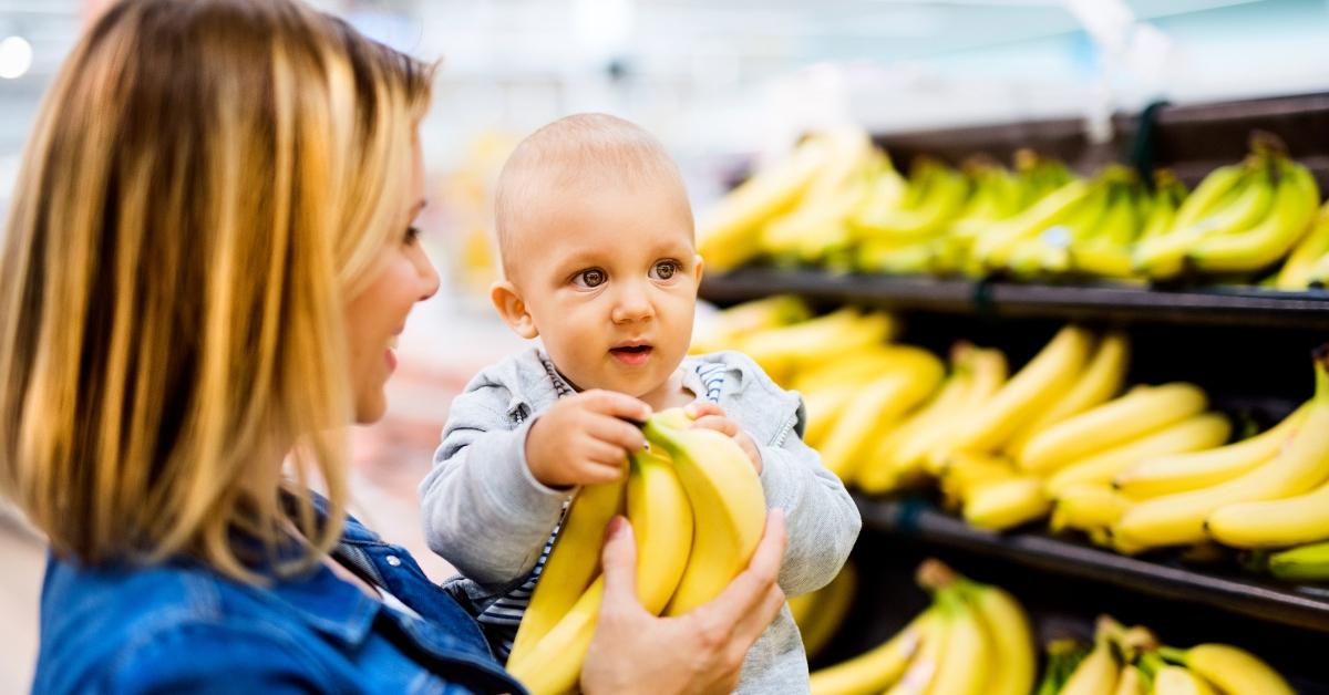 A woman and a baby with bananas at the store. 