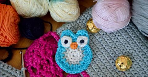 A small blue and white crocheted owl surrounded by various colors of yarn and a crochet hook.