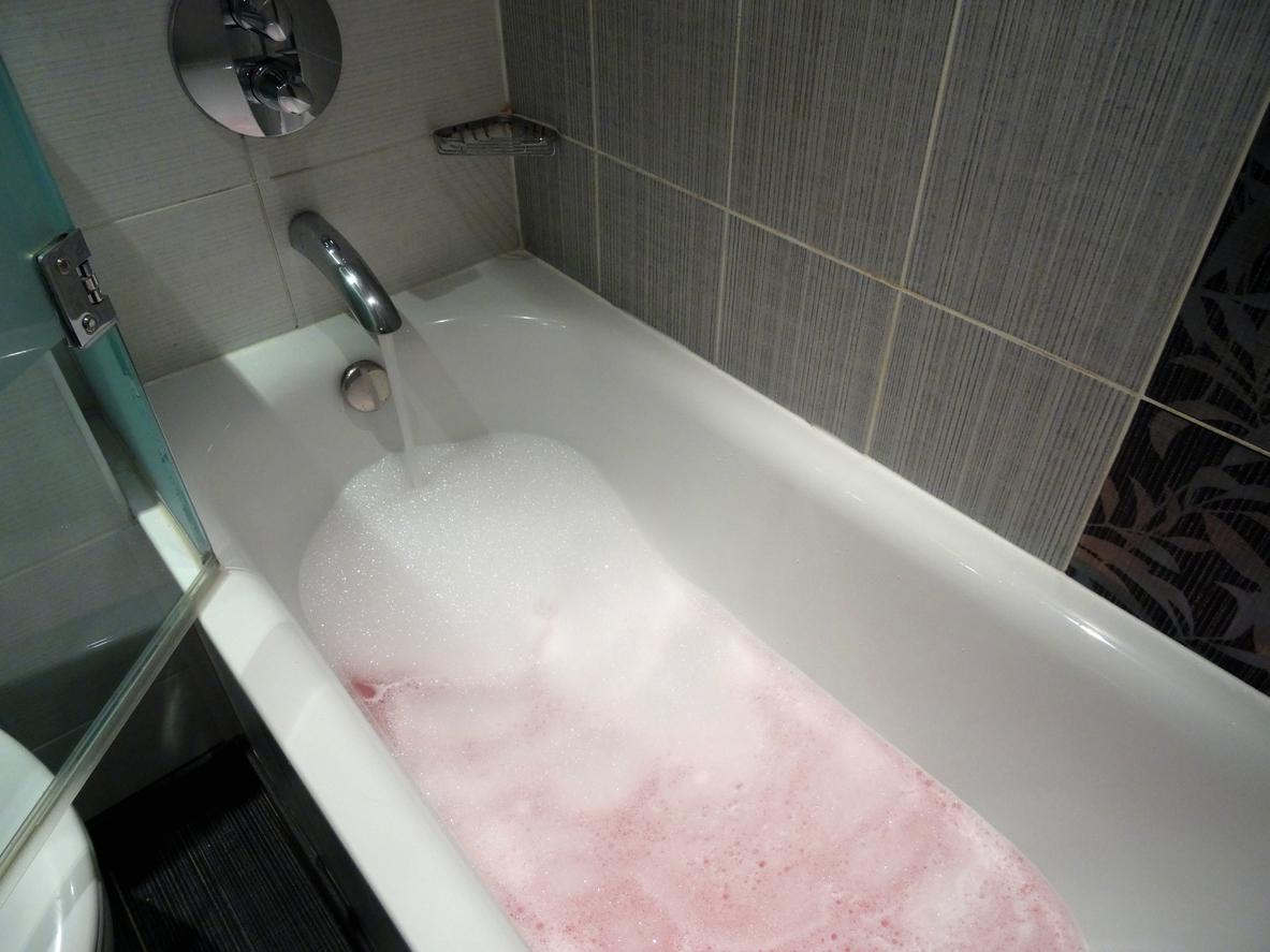 White bathtub filling up with water and bubbles.