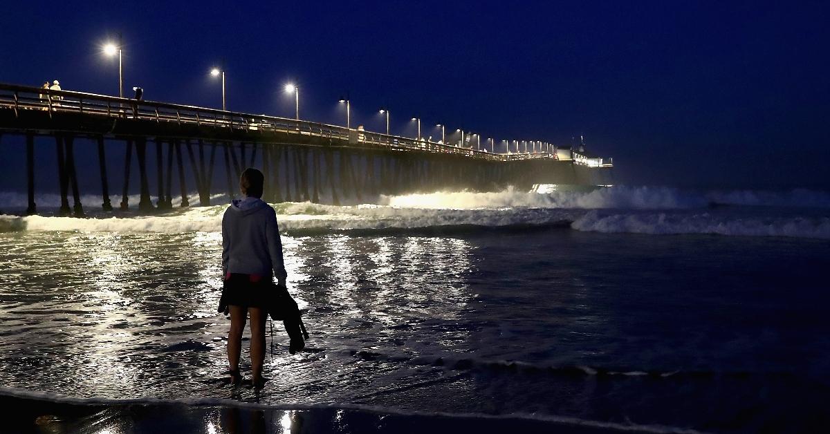 A man stands by the Imperial Beach pier at night watching the waves.