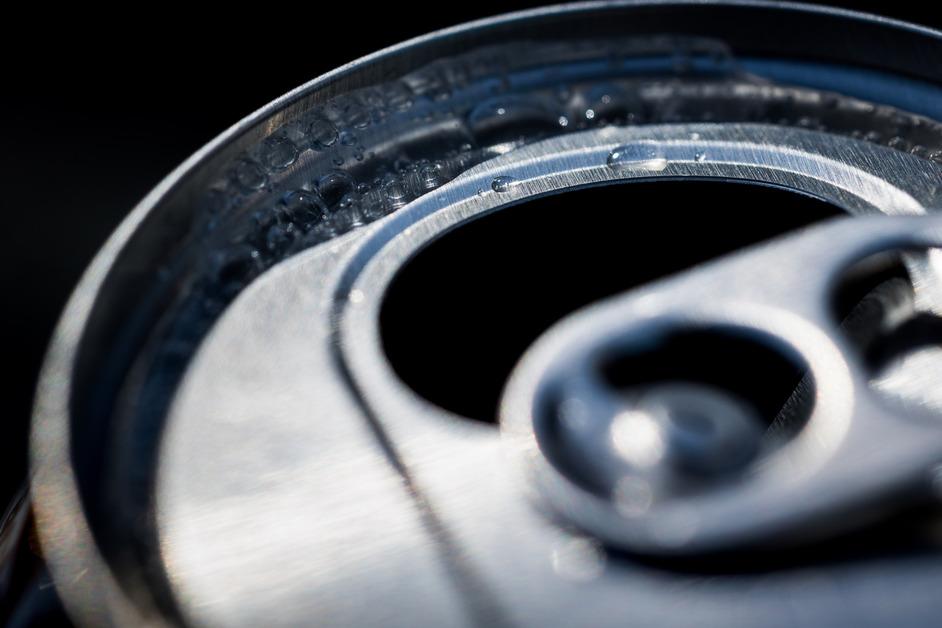 A close up of a can containing a carbonated drink with bubbles gather around the rim. 