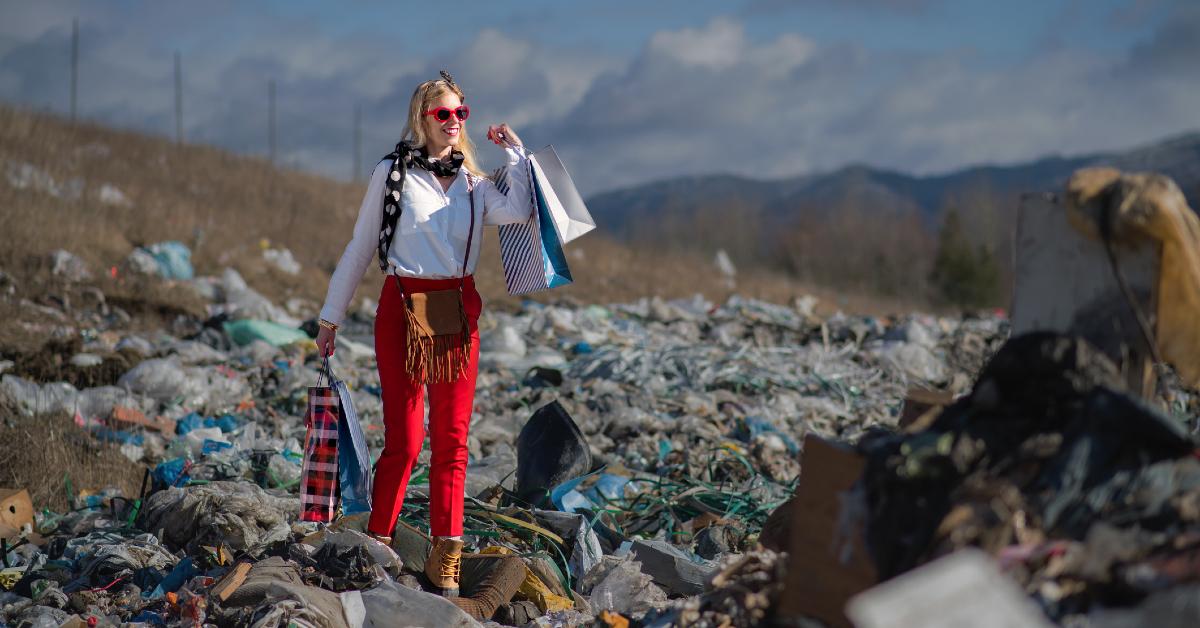 Woman holding shopping bags while smiling and standing in a landfill 