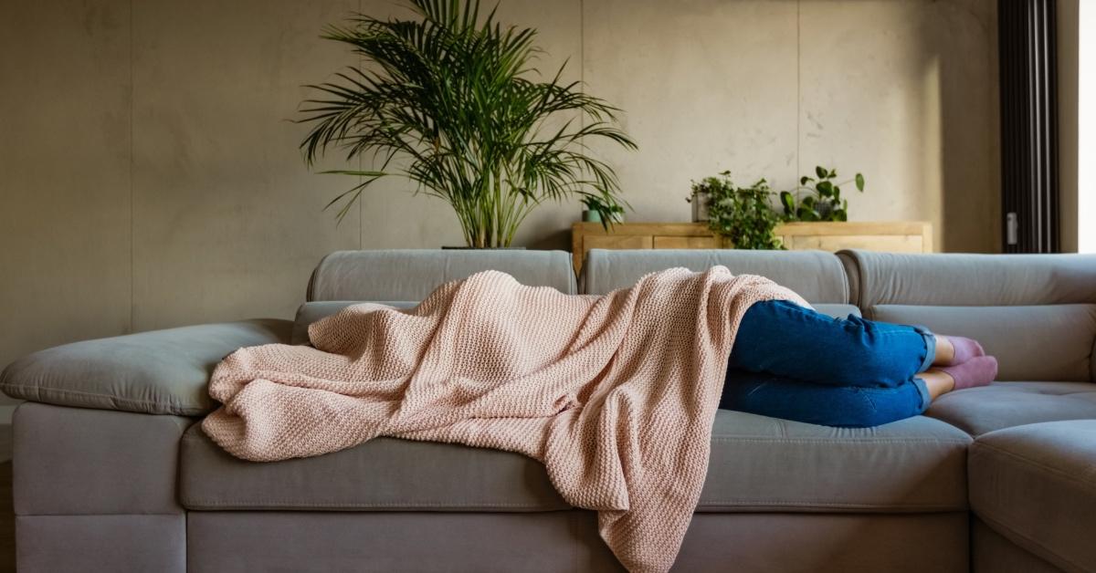 Person laying on the couch with their head under a blanket. 