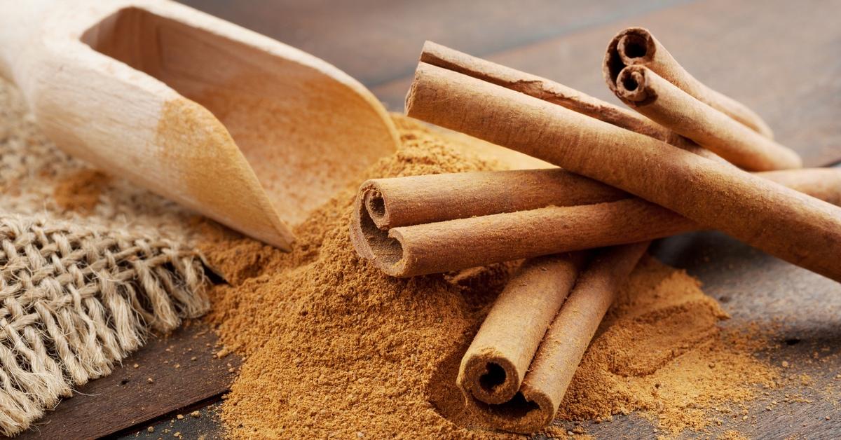 Cinnamon sticks atop cinnamon powder with a wooden scoop.