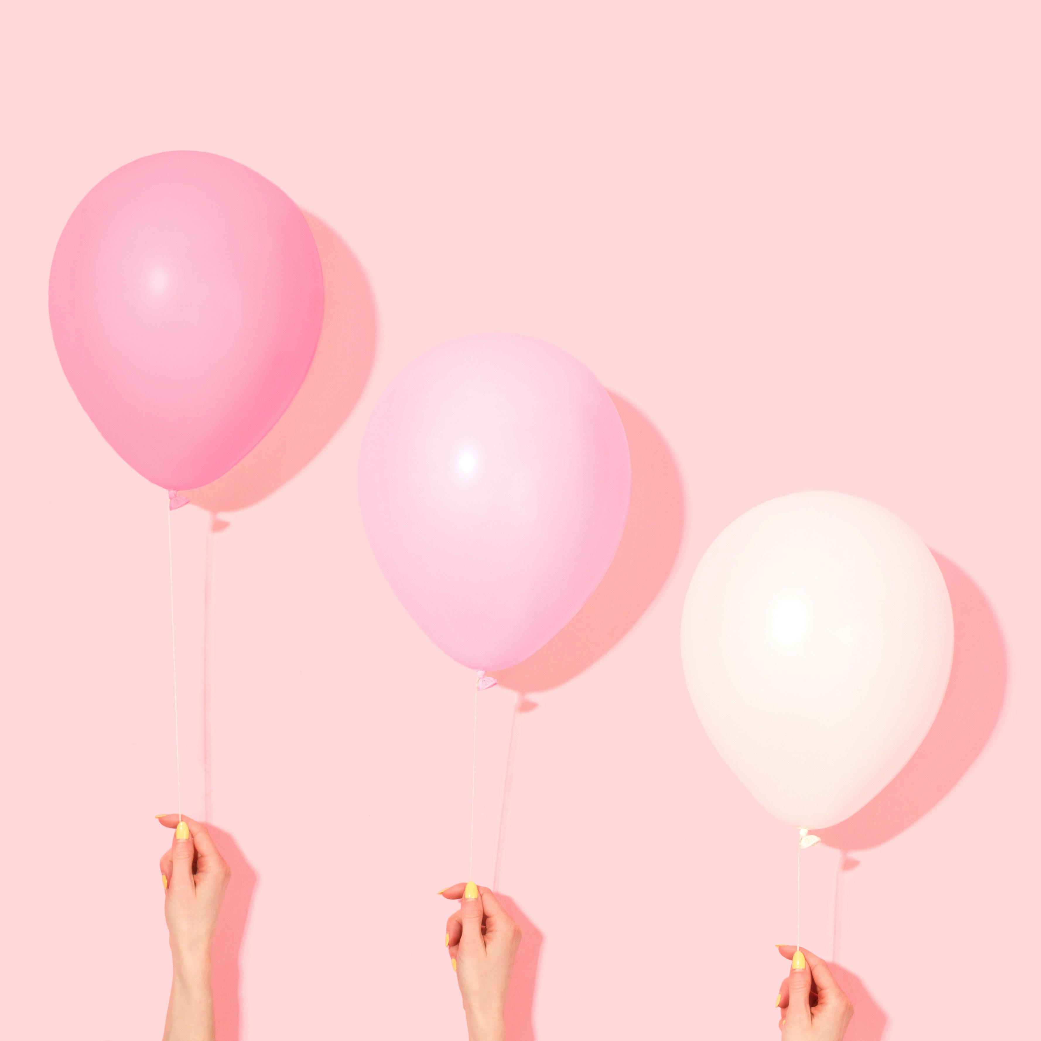 Three balloons of different shades of pink are held at varying heights against a pink background.