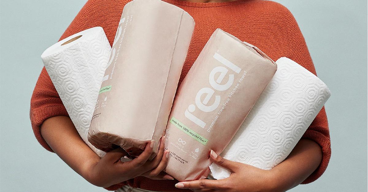 a woman's arms holding four rolls of Reel paper towels