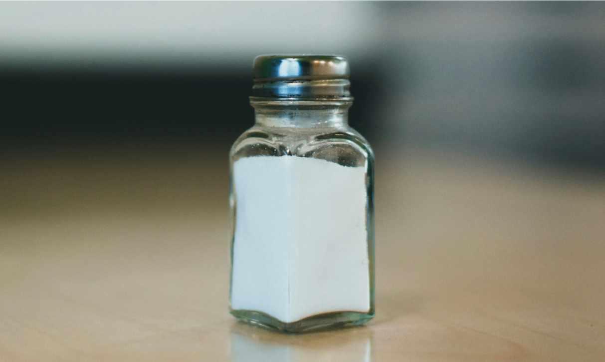 A salt shaker is pictured atop a wooden table.