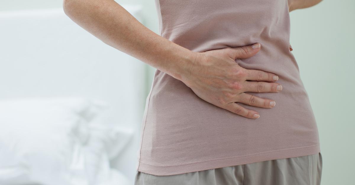 Someone holds their stomach, wearing a pink shirt and grey sweatpants.