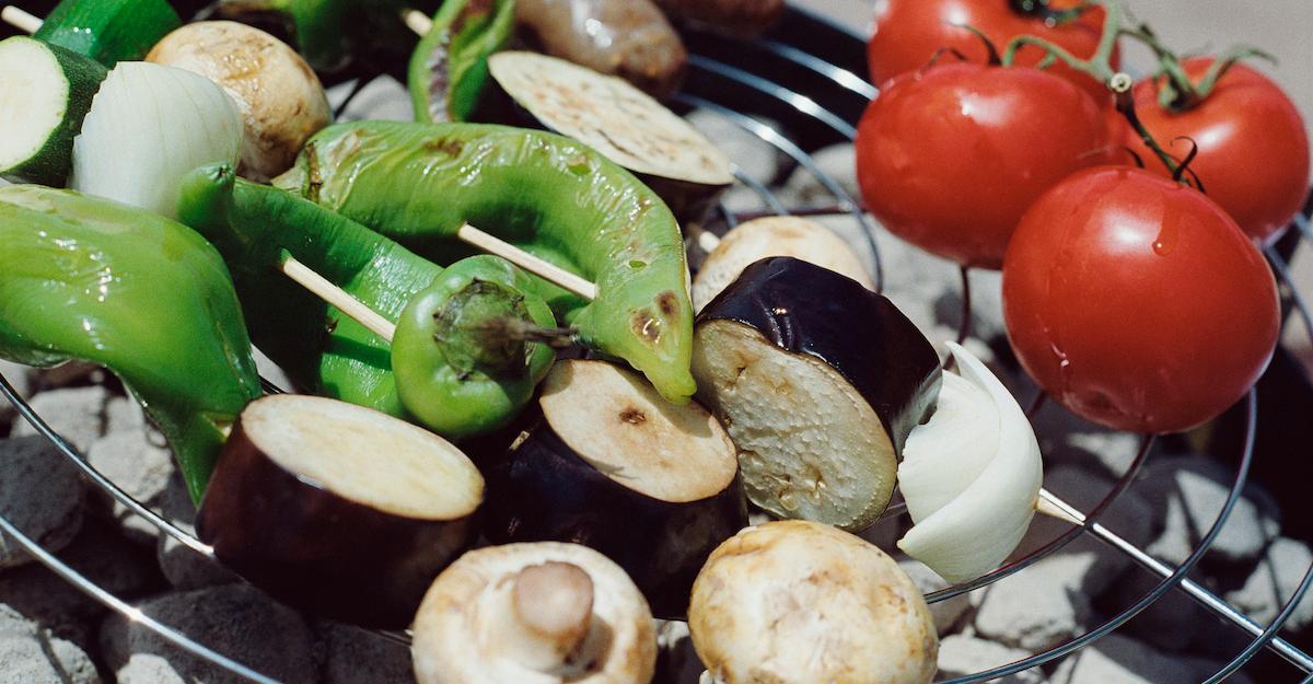 Close-up photograph of vegetables on a grill, including peppers, mushrooms, and tomatoes.