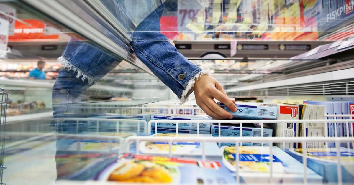 A woman reaches into a freezer containing ready-to-eat products at the grocery store