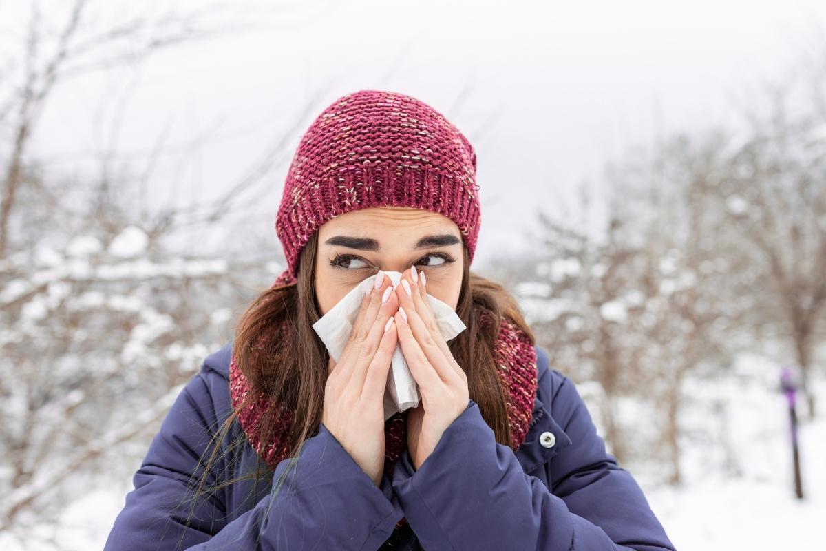 Woman in blue coat and maroon cat uses a tissue in the snow