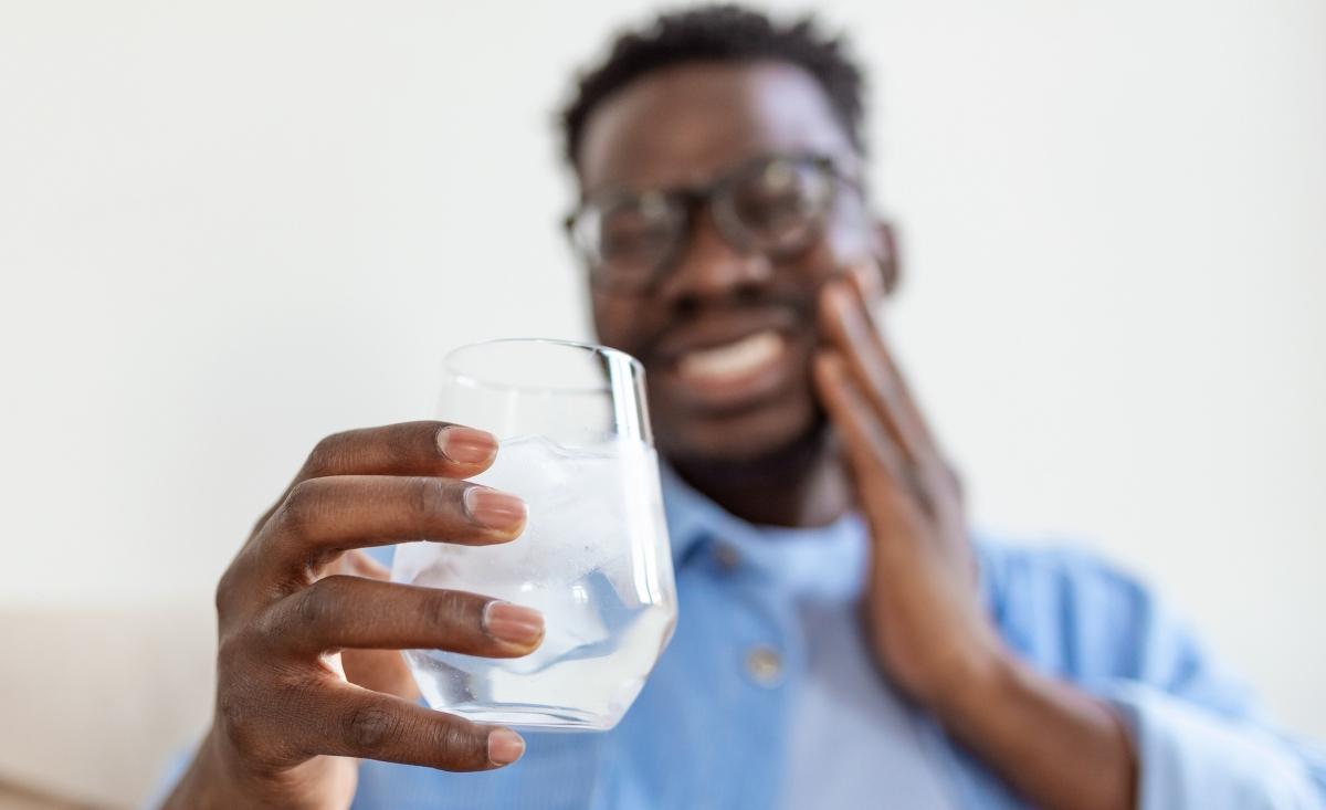 Black man touching jaw in pain and holding glass of ice water